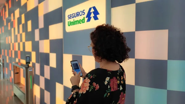 Fotografia colorida de uma mulher com a carteirinha da Unimed aberta