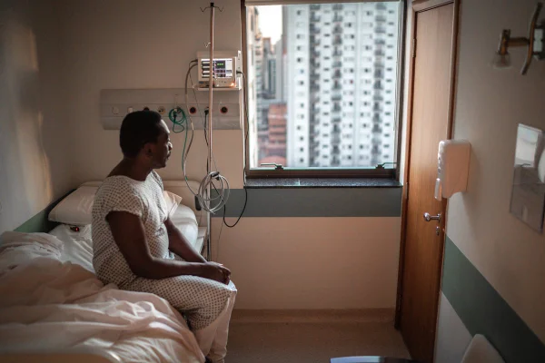 Fotografia colorida. homem sentado em cama de hospital olha pela janela - câncer de próstata