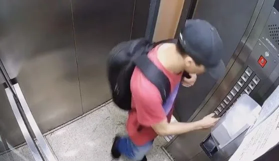 Imagem colorida mostra Davi Izaque Martins Silva, um homem branco, magro, vestido com uma camiseta vermelha e um boné preto, com uma mochila preta nas costas, apertando o botão de um elevador, em imagem feita por câmeras de segurança - Metrópoles