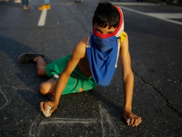 Um jovem manifestante escreve slogans na calçada durante protesto contra o governo de Nicolás Maduro nas ruas de Caracas, em 2 de fevereiro de 2019 - Metrópoles