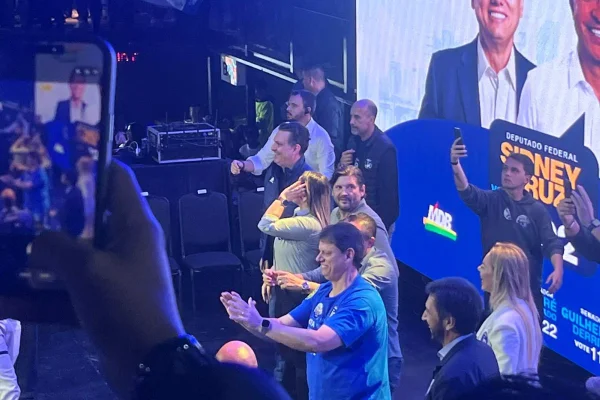 Imagens coloridas mostram o governador Tarcísio de Freitas batendo palmas sobre palco durante evento de campanha