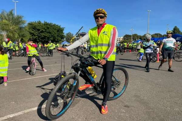 Homem de capacete, sentado em bike, veste colete amarelo