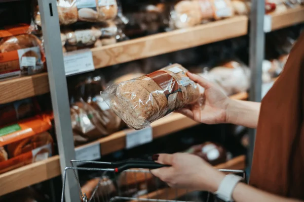 Jovem asiática carregando um carrinho de compras fazendo compras em um supermercado, comprando pão integral fresco embalado no corredor do pão. Estilo de vida de alimentação saudável
