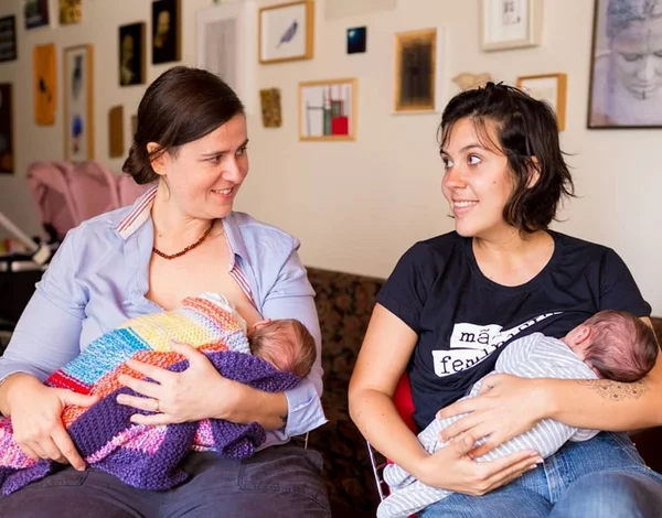 Casal homoafetivo se olhando enquanto amamentam os filhos gêmeos