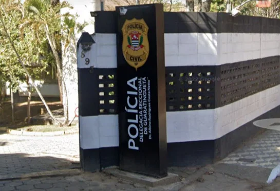 Imagem colorida mostra placa que sinaliza entrada da Delegacia Seccional de Guaratinguetá; paredes são pintadas em listrado (preto e branco) - Metrópoles