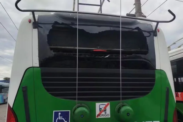 Traseira de ônibus, nas cores branco e verde, com vidro quebrado - Metrópoles