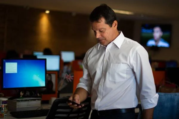 Homem de camisa olha para celular em sua mão direita