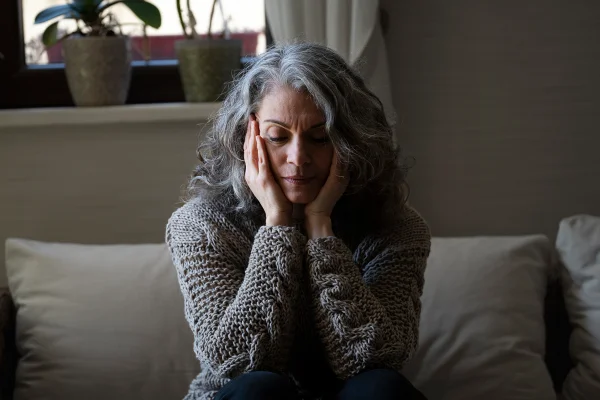 Mulher mais velha sentada no sofá. Dor de cabeça, alzheimer, nevoa mental, menopausa. Metrópoles