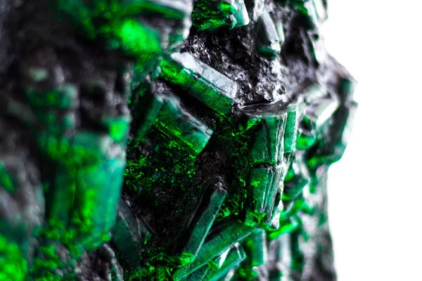 Imagem colorida mostra cristais de esmeralda esverdeados em pedra escura que será leiloada. Metrópoles