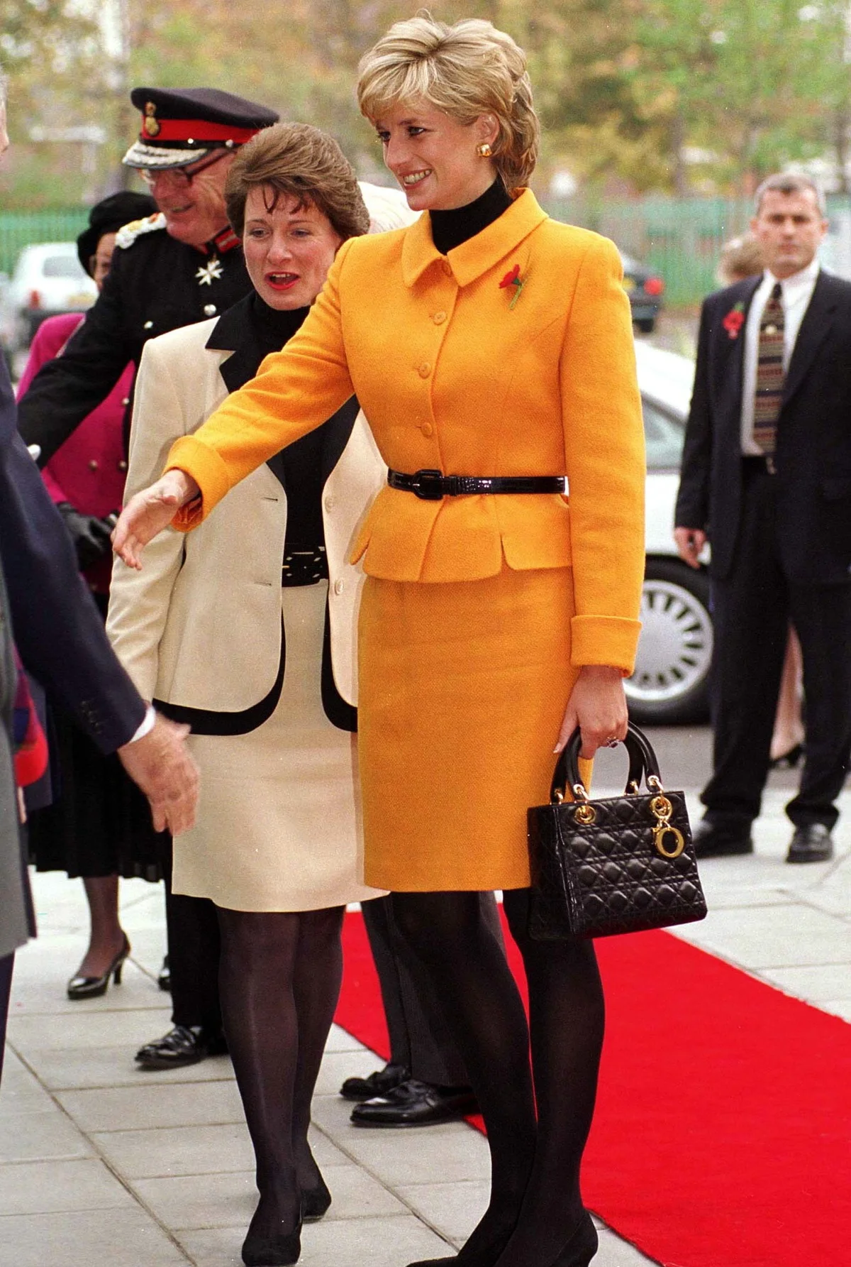 Diana vestindo um conjunto laranja vibrante, assinado pela Versace, e carrega uma bolsa da Dior Diana vestindo um conjunto laranja vibrante, assinado pela Versace, e carrega uma bolsa da Dior