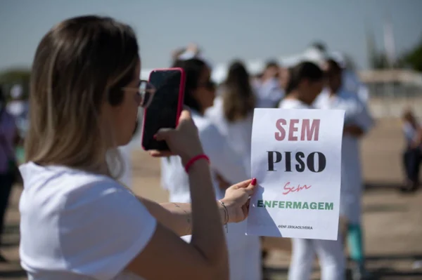 Mulher tira foto de cartaz escrito "Sem piso, sem enfermagem"