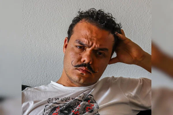 Imagem colorida de Carlos Candreva. Ele está de bigode e com a mão apoiada na cabeça - Metrópoles