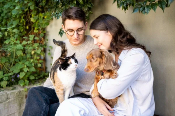 Imagem colorida de casal segurando um gato e um cachorro no colo