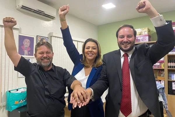 Fotografia colorida de três pessoas dando as mãos
