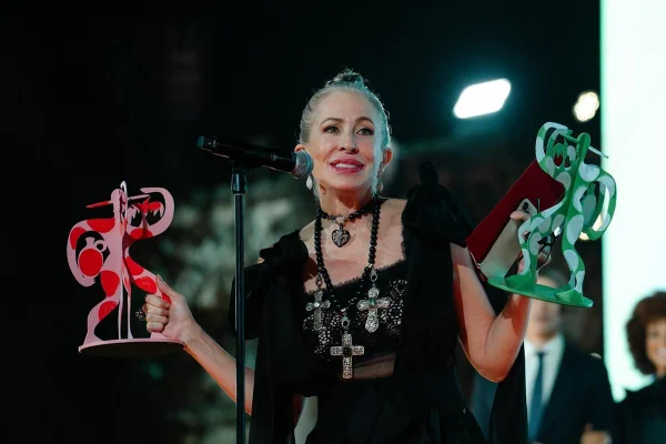Em palco de premiação, mulher segura dois troféus coloridos - Metrópoles
