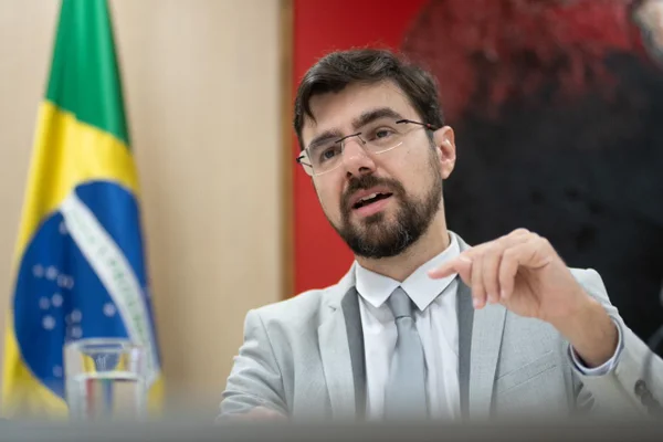 Foto colorida do secretário Guilherme Mello, à frente de bandeira do Brasil - Metrópoles