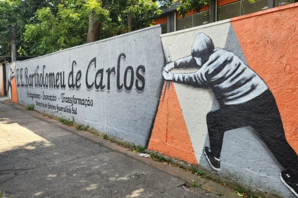 imagem colorida mostra fachada de escola. na parede está escrito o nome escola bartholomeu de carlos e há dois desenhos de pessoas