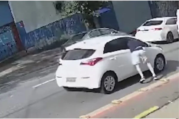 Em imagem colorida homem coloca metade do corpo dentro de janela do passageiro de carro - Metrópoles
