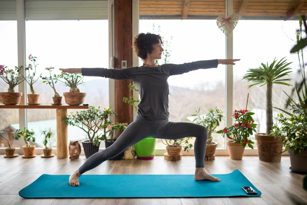 Mulher madura muito bonita se exercitando e praticando ioga em casa, no pátio, com bastante luz, em um dia nublado de inverno. Ela parece muito em forma, magra e perfeitamente flexível. Metrópoles