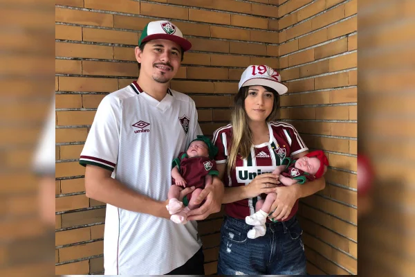 Imagem colorida de casal com camisa do Fluminense segurando filhas no colo - Metrópoles
