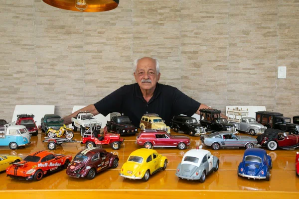 Homem posa com carrinhos em mesa de madeira