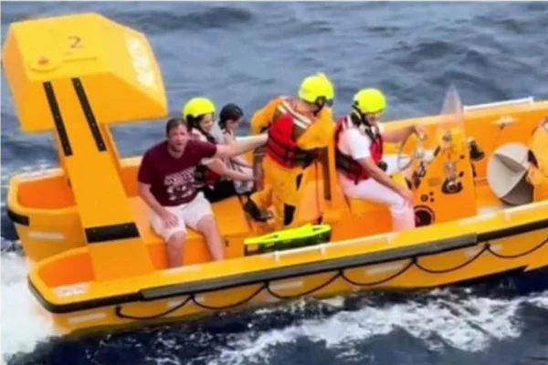Foto colorida de pai e criança sendo resgatados por tripulantes do navio da Disney - Metrópoles