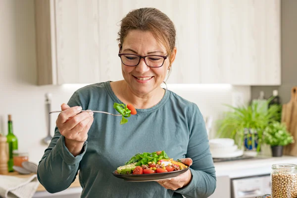 Foto colorida de mulher segurando garfo e prato com salada - Metrópoles