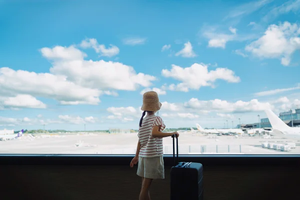 Imagem mostra criança com mala e chapéu de viagem no aeroporto, olhando os aviões - Metrópoles