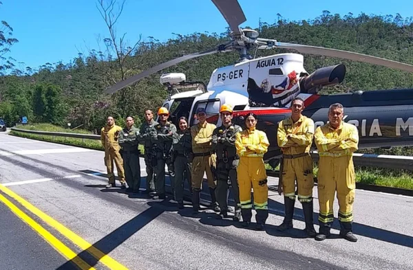 Imagem colorida mostra integrantes do Corpo de Bombeiros na frente de um helicóptero após resgate de um turista perto da Rodovia Mogi-Bertioga - Metrópoles