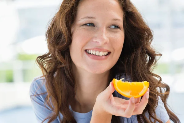 Foto colorida de mulher comendo laranja - Metrópoles