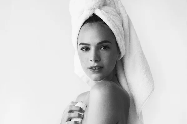 A atriz brasileira Bruna Marquezine, uma mulher jovem e branca, de cabelo liso castanho, posa para foto em um fundo branco. Ela usa uma toalha branca amarrada à cabeça e uma outra toalha para cobrir o corpo. Ela está, portanto, seminua. O retrato é do fotógrafo Mario Testino. - Metrópoles