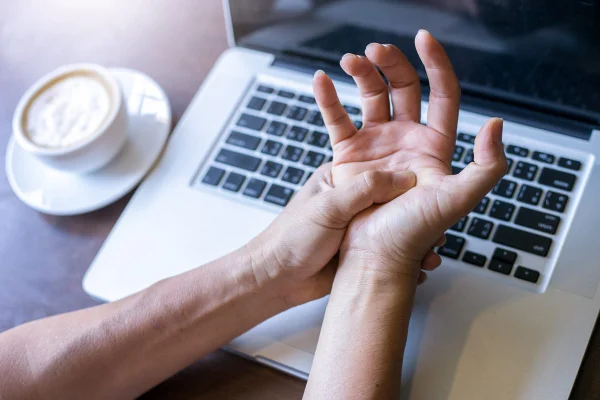 Pessoa apertando a mão com dor em frente a um teclado - Metrópoles