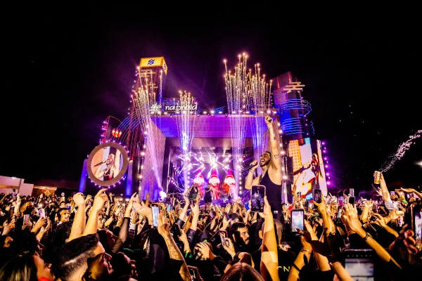 foto colorida do festival na praia com um show no fundo a noite
