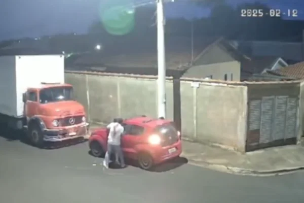 Imagem colorida de uma câmera de rua que mostra um homem assaltando uma mulher contra um carro vermelho - Metrópoles