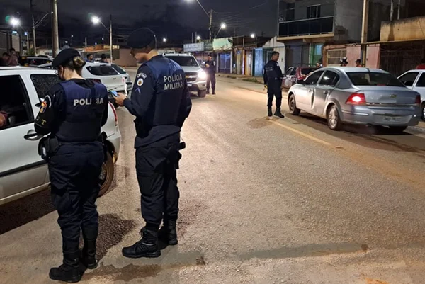 Policiais militares ao lado de carros em pista, à noite
