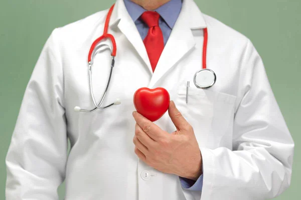 Médico com equipamentos e jalecos segurando um coração de borracha no peito