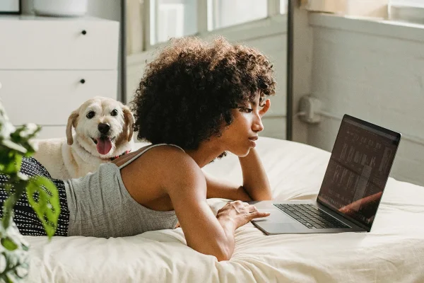 Jovem mulher negra deitada em cama de frente para tela de laptop - Metrópoles