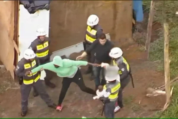 Imagem colorida de mulher de blusa verde cercadas de policiais militares. Metrópoles
