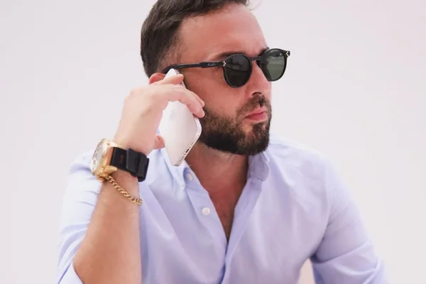 Irmão de Virginia Fonseca, William Gusmão posa de camisa social branca, óculos escuros e segurando um telefone celular - Metrópoles