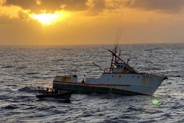 Foto colorida de pesqueiro em alto mar, com sol entre nuvens de fundo - Metrópoles
