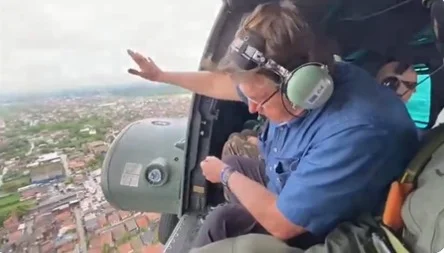 Bolsonaro sobrevoa Recife de helicóptero, acenando para as pessoas embaixo. É possível ver parte da cidade - Metrópoles