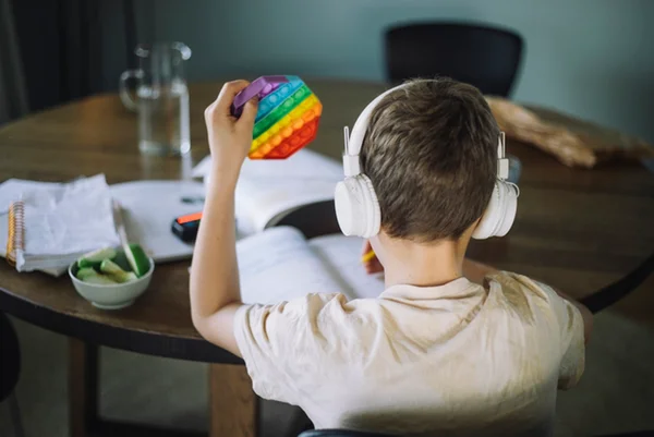 Foto colorida de menino de costas com fone de ouvido branco segurando brinquedo colorido - Metrópoles