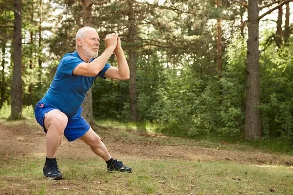 Idoso com barba vestido de azul faz exercício ao ar livre em área verde - Metrópoles