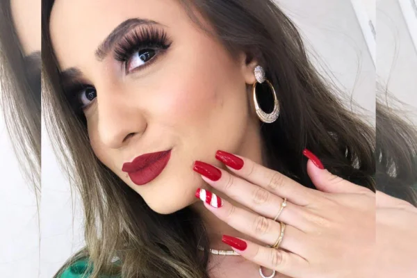Foto colorida. Mulher banca com o batom vermelho, cílios postiços e unhas vermelhas