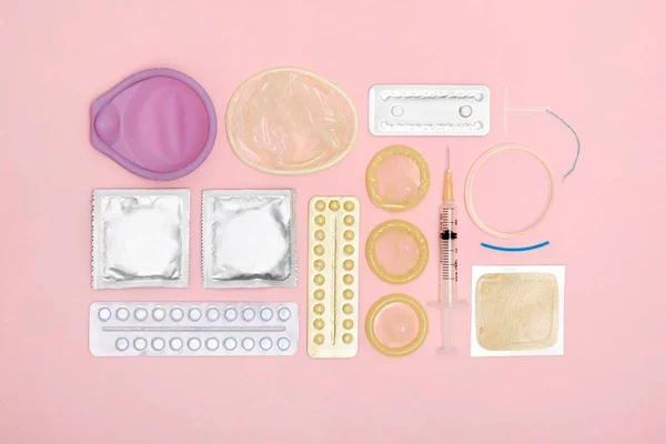 Foto de fundo rosa com objetos como camisinhas, pílulas e seringas espalhadas - Metrópoles