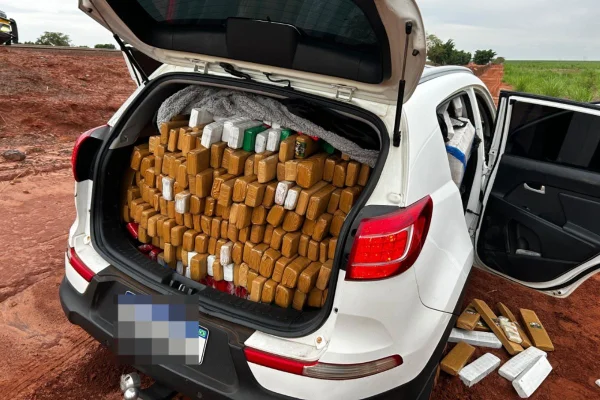 Imagem colorida mostra carro branco com porta-malas aberto. Dentro estão diversos pacotes embrulhados em formato de tijolo, empilhados - Metrópoles