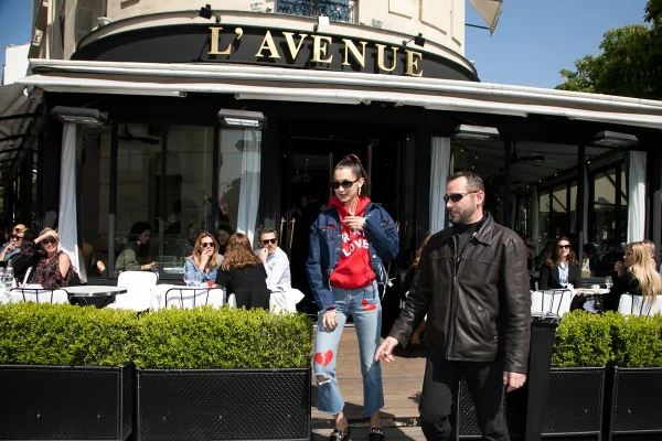 Foto colorida de mulher branca saindo ao lado de segurança de um lugar chamado L'Avenue - Metrópoles