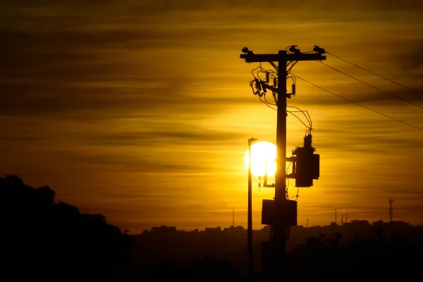 Imagem em tons amarelos de um poste de energia e, ao fundo, o pôr-do-sol.