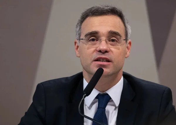 Ministro Fotografia colorida do ministro do STF André Mendonça. Ele é um homem branco, de meia idade, com cabelos curtos, grisalhos nas laterais e preto no centro. Usa óculos sem armação visível.
