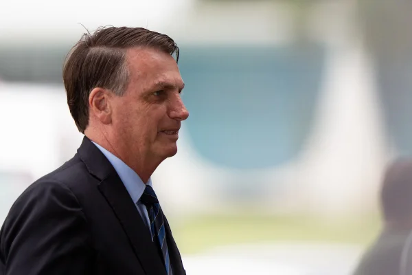 Fotografia colorida. Bolsonaro aparece de perfil, à esquerda da imagem, vestindo paletó. A foto foi tirada no Palácio da Alvorada